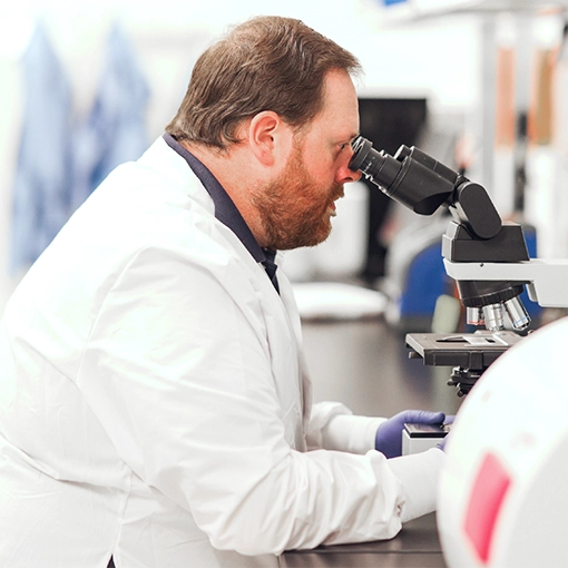 A laboratory scientist examines a sample through a microscope.